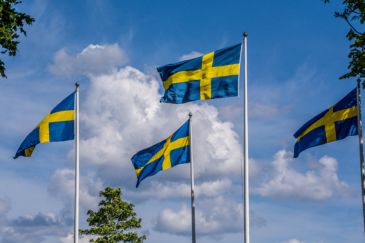 Svenska flaggor mot blå himmel.