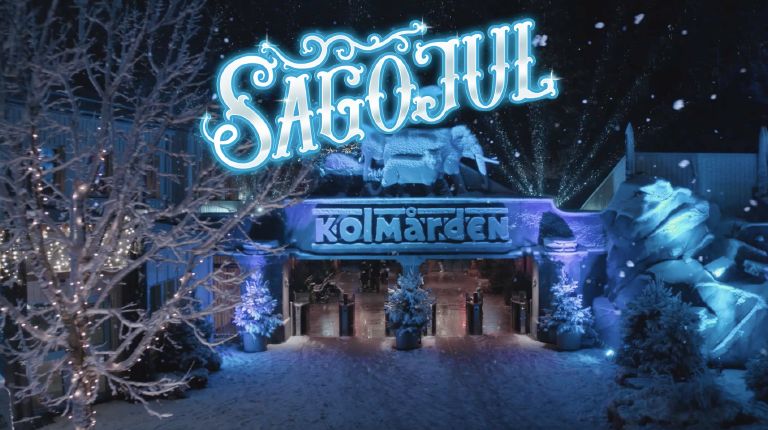 Kolmårdens entré, blått ljus, snö. Texten "Sagojul" och Kolmårdens logotyp.